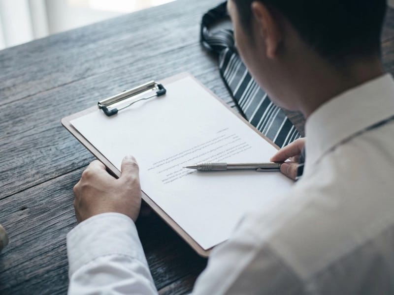 Man in a white shirt holding a pen over a document on a clipboard