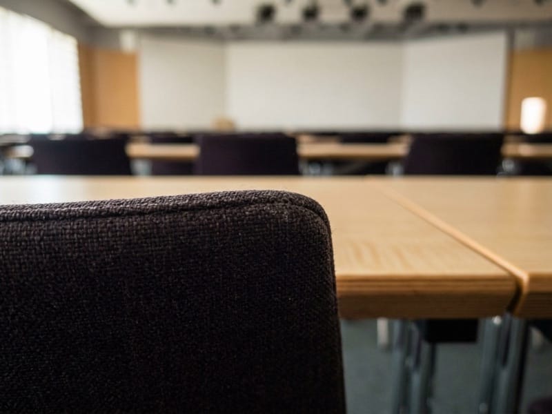 Empty seminar room with rows of wooden tables, chairs and a whiteboard